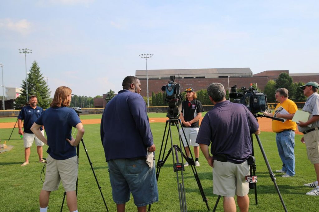 People standing around cameras on a baseball field.