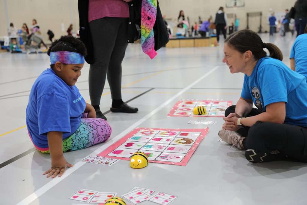 Teacher sitting on floor with student playing with bee bots