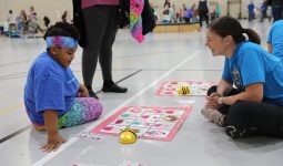 Teacher sitting on floor with student playing with bee bots