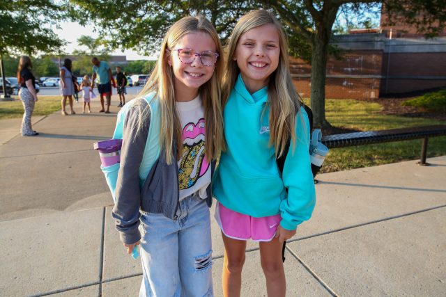 two elementary grade female students with backpacks smiling arriving for school
