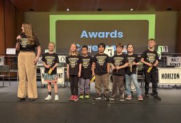 Children standing on stage in front of podiums at an awards ceremony.
