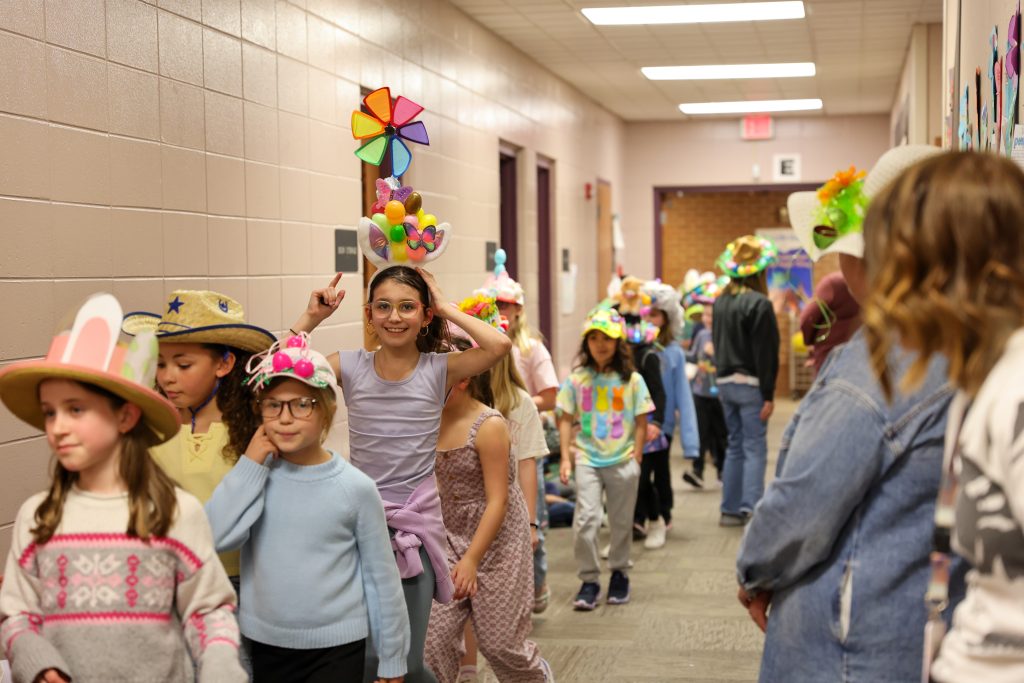 Children wearing party hats walking down hallway pose for a picture