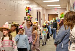 Children wearing party hats walking down hallway pose for a picture