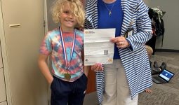 Woman holding a medal with a boy beside her. They are in an office setting.