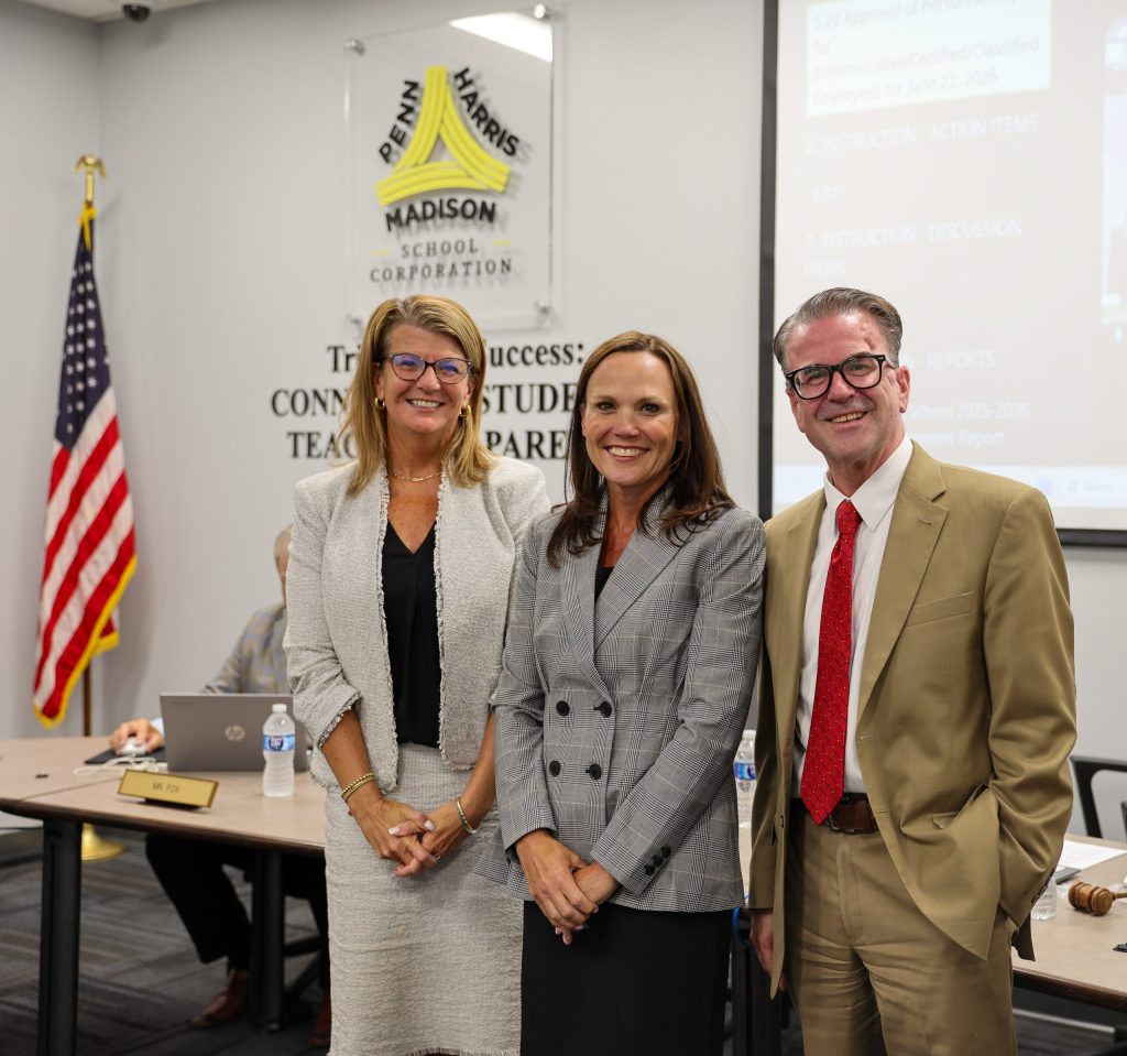 Three people standing in front of a podium at an event. The person on the left is wearing glasses and a red top. The middle