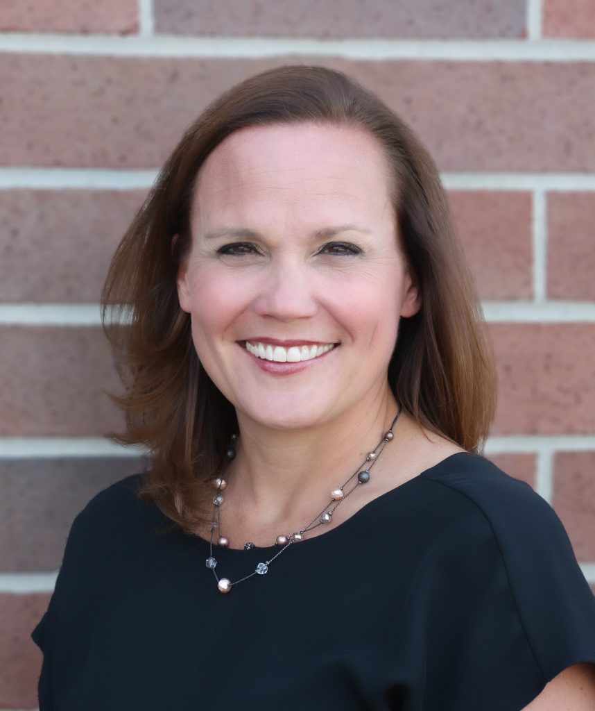 Woman posing against brick wall, smiling at camera.