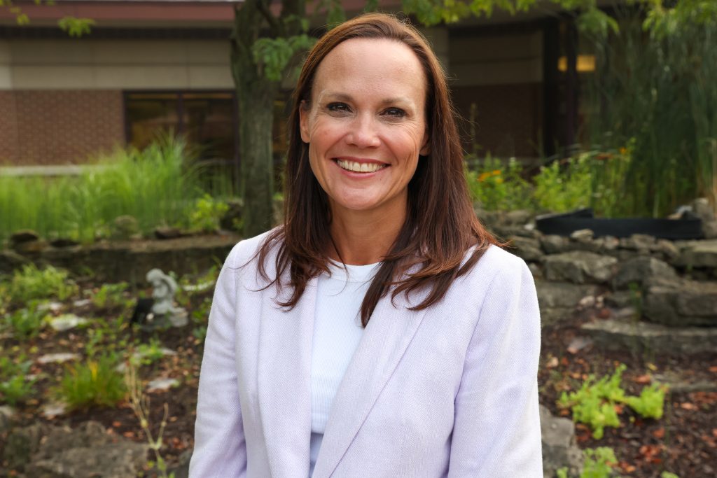 Woman standing in front of a building, smiling at the camera.