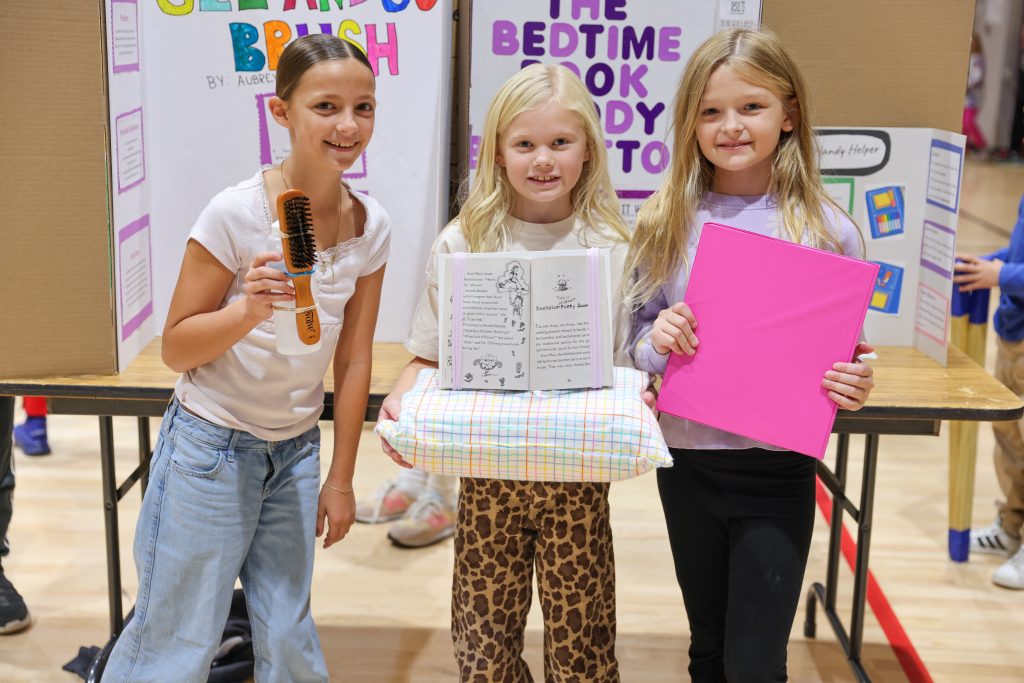 Three young girls proudly displaying their projects at a science fair.
