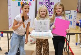 Three young girls proudly displaying their projects at a science fair.